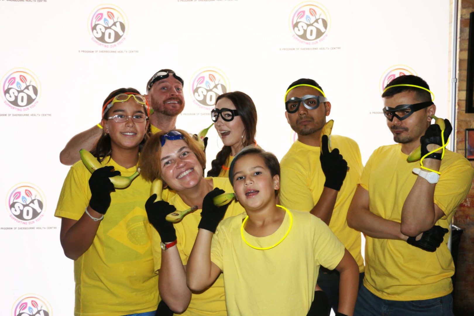 a group of people dressed as minions, wearing yellow, wearing yellow glow bracelets and glasses while holding bananas