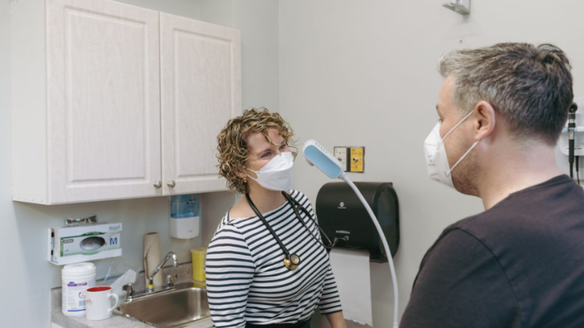 A nurse practitioner speaks with a service user in an exam room.