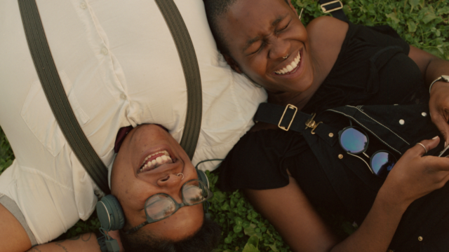 Two Black youth lying down on a grassy area.