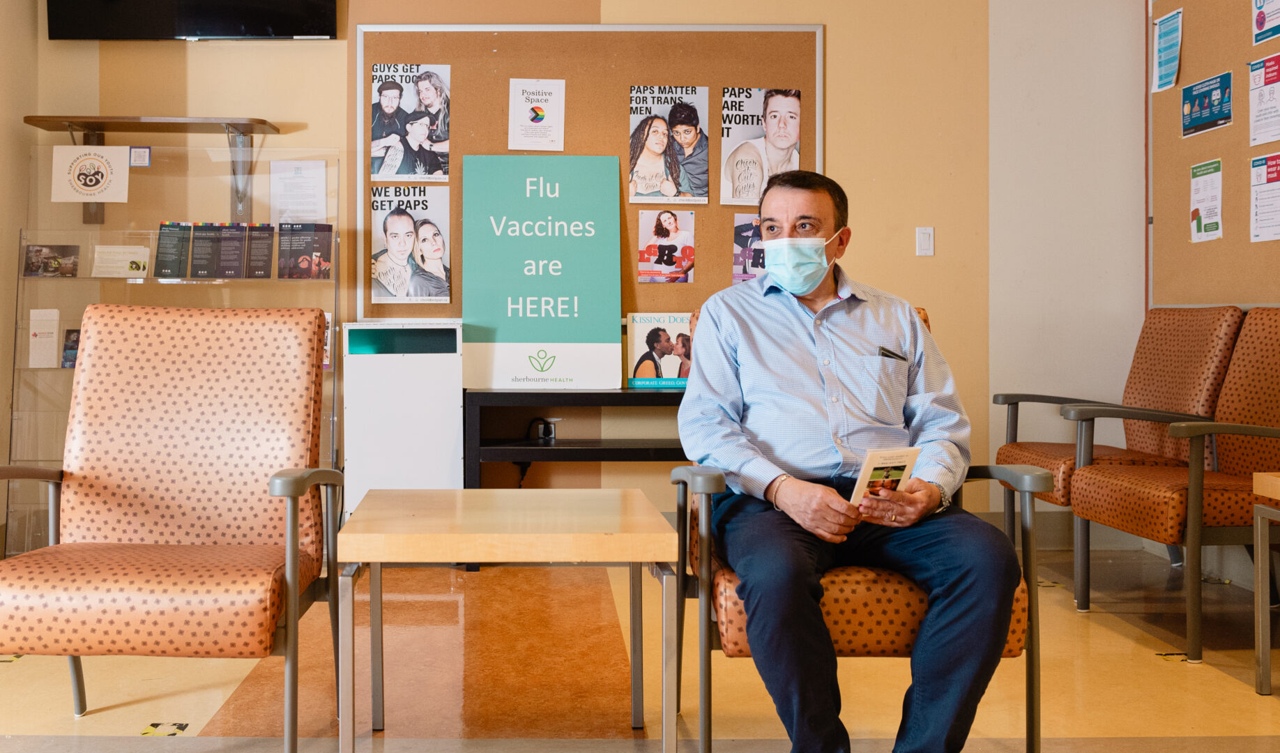 A client sitting in a waiting room at Sherbourne Health Centre. Behind them is a poster sign that reads, 
