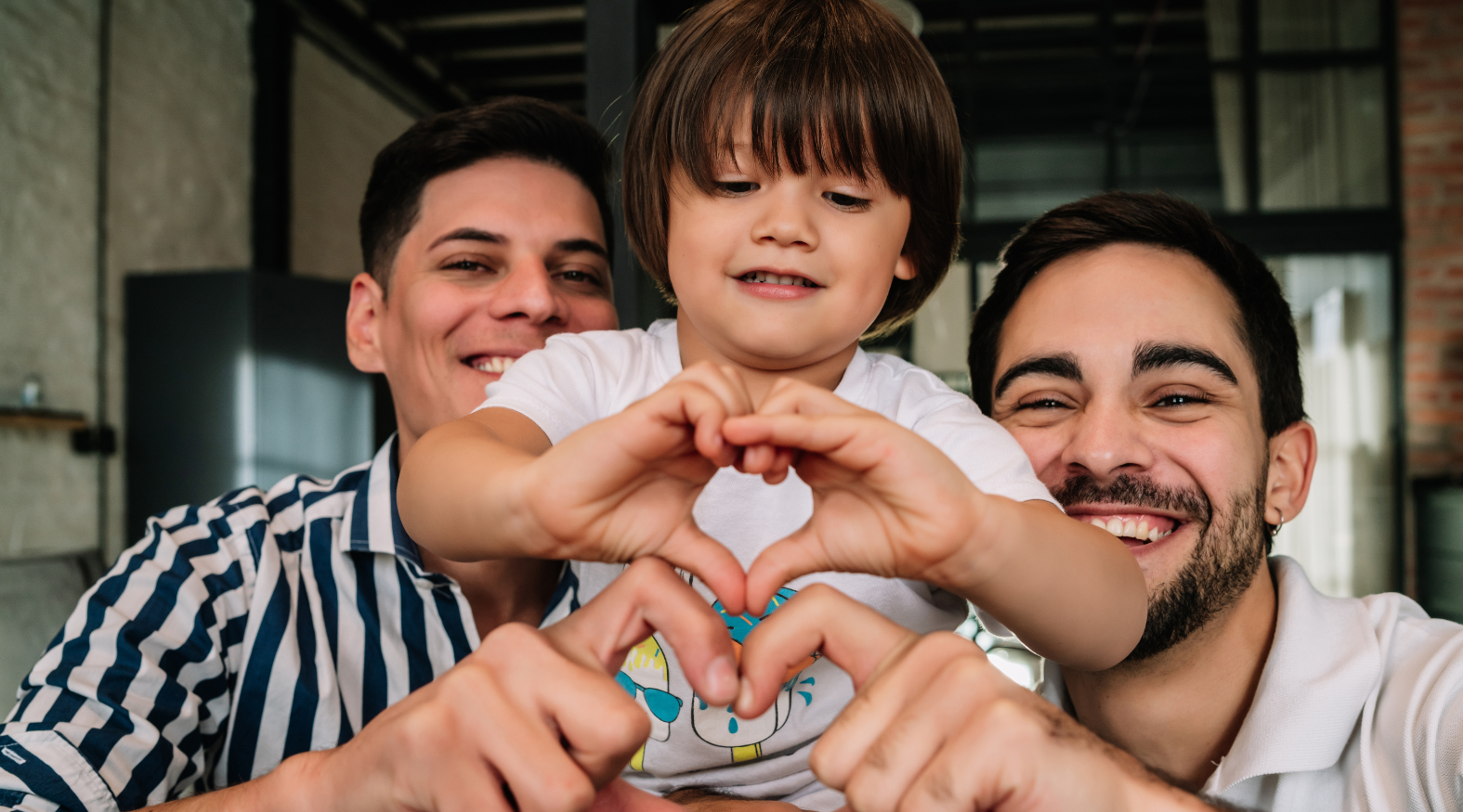 Queer parents and their child making a heart shape with their hands.
